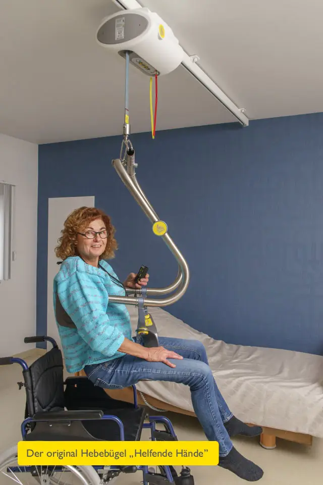 Deckenlifter Handi-Move – selbstständiger Transfer vom Rollstuhl: Frau im Hebebügel über dem Rollstuhl, hat die Fernbedienung in der Hand